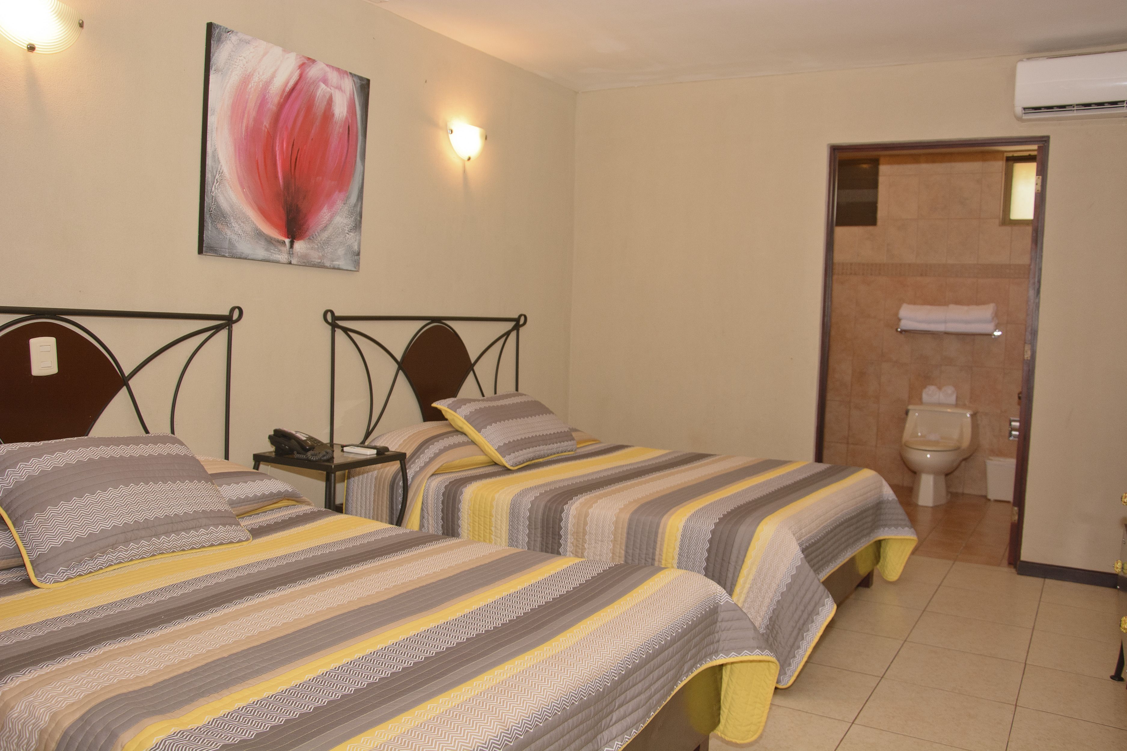 A hotel room with two beds, a painting on the wall, and a bathroom visible through an open door.
