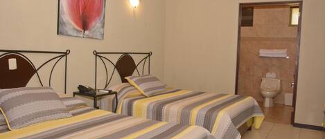 A hotel room with two beds, a painting on the wall, and a bathroom visible through an open door.