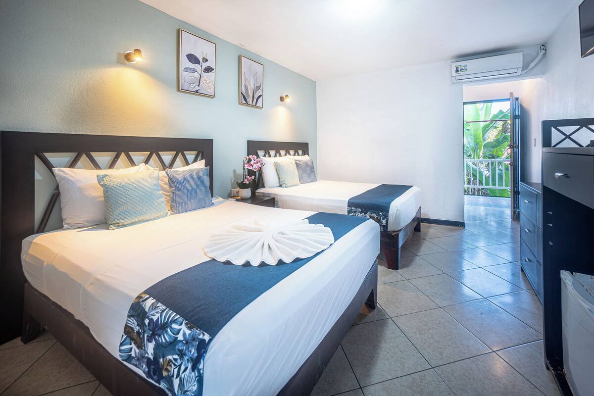 A hotel room with two beds, a balcony, a dresser, and wall-mounted artwork.