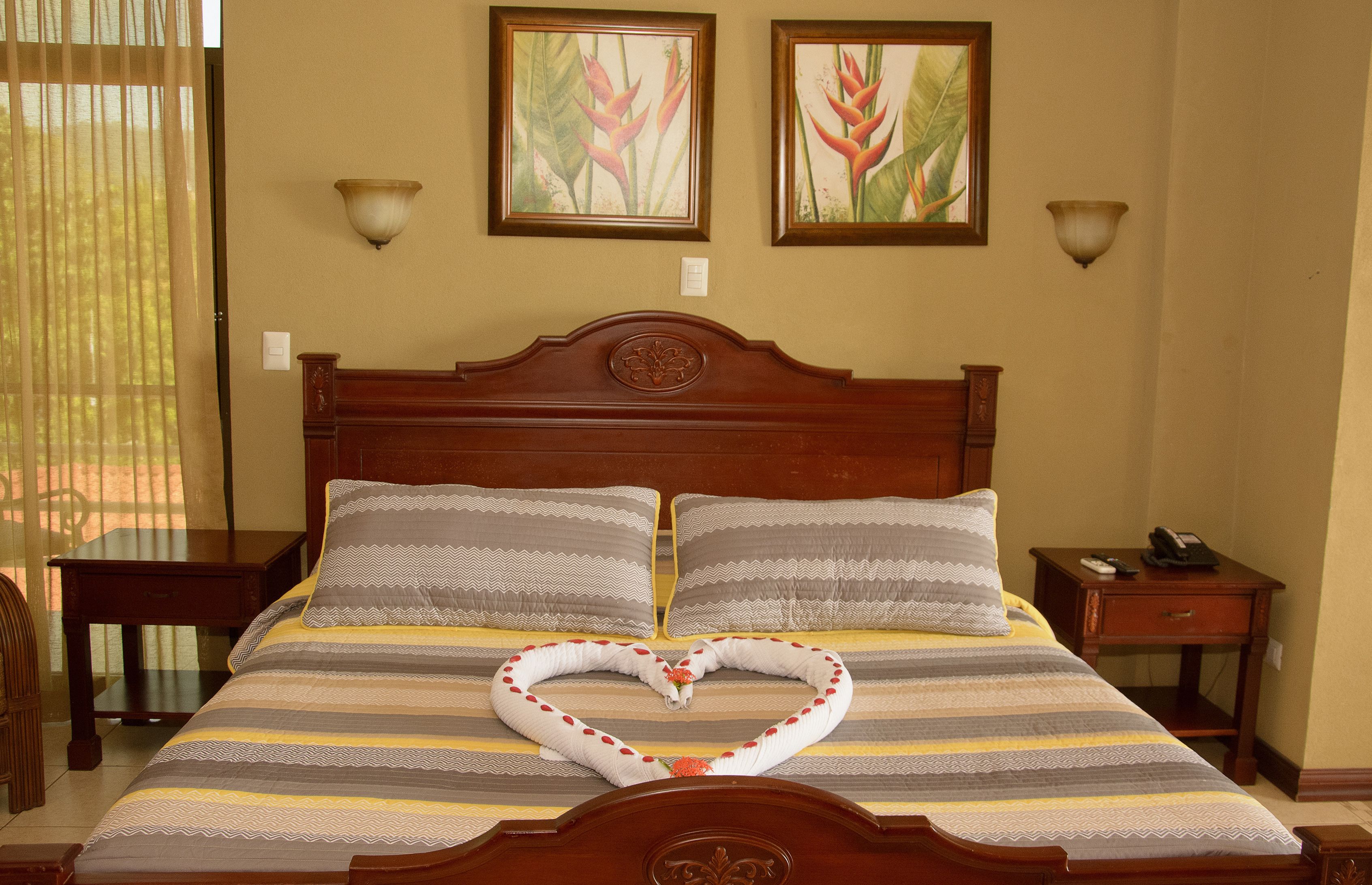 A neatly made bed with striped bedding, two wall-mounted lamps, and two framed botanical paintings.