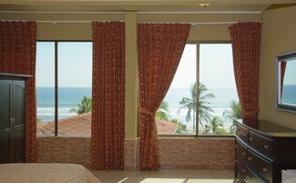 Quarto com uma grande janela com vista para o oceano, uma cama, uma cômoda e uma televisão.