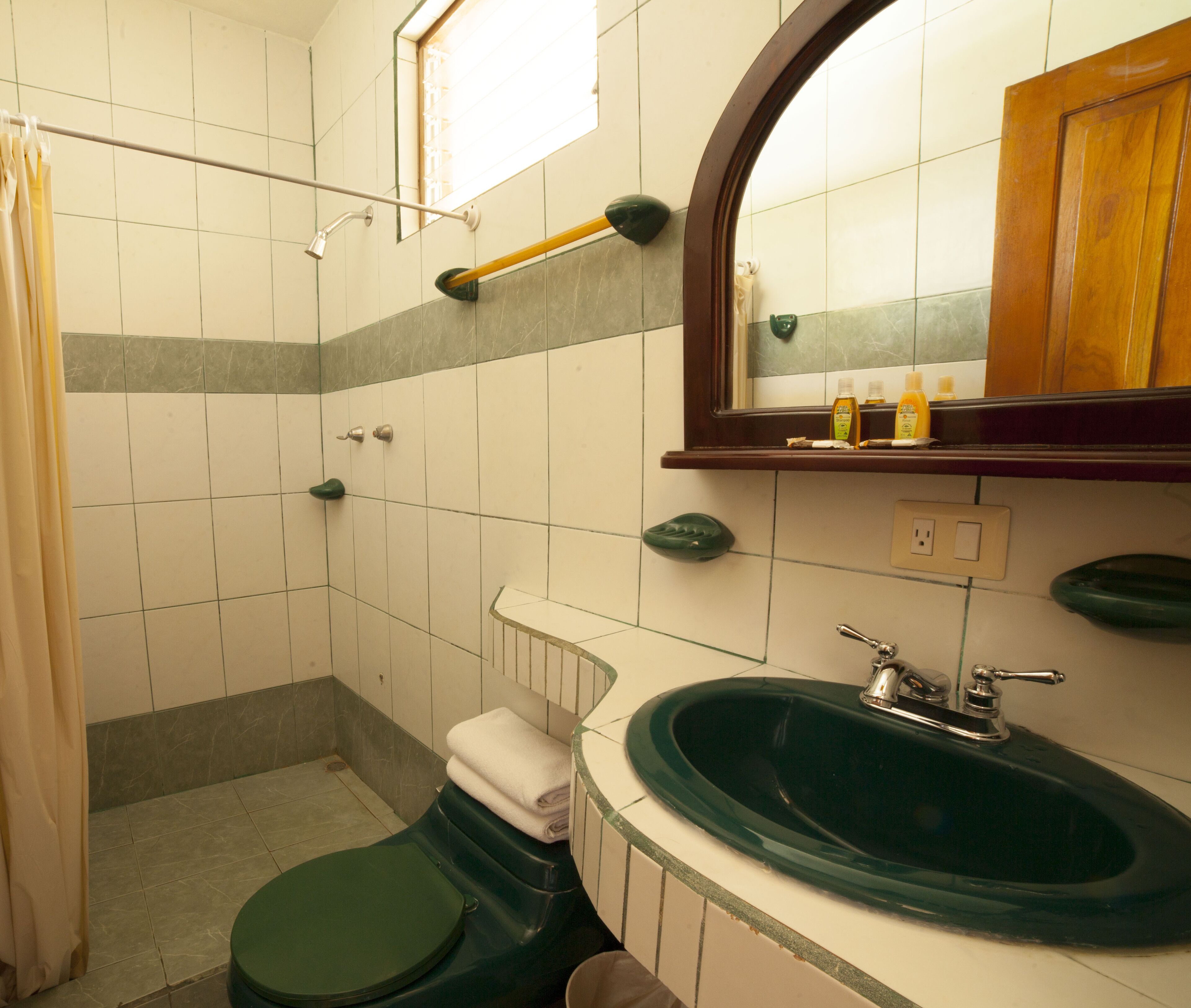 A bathroom with a green toilet, a sink with a green basin, a mirror, and a shower area.