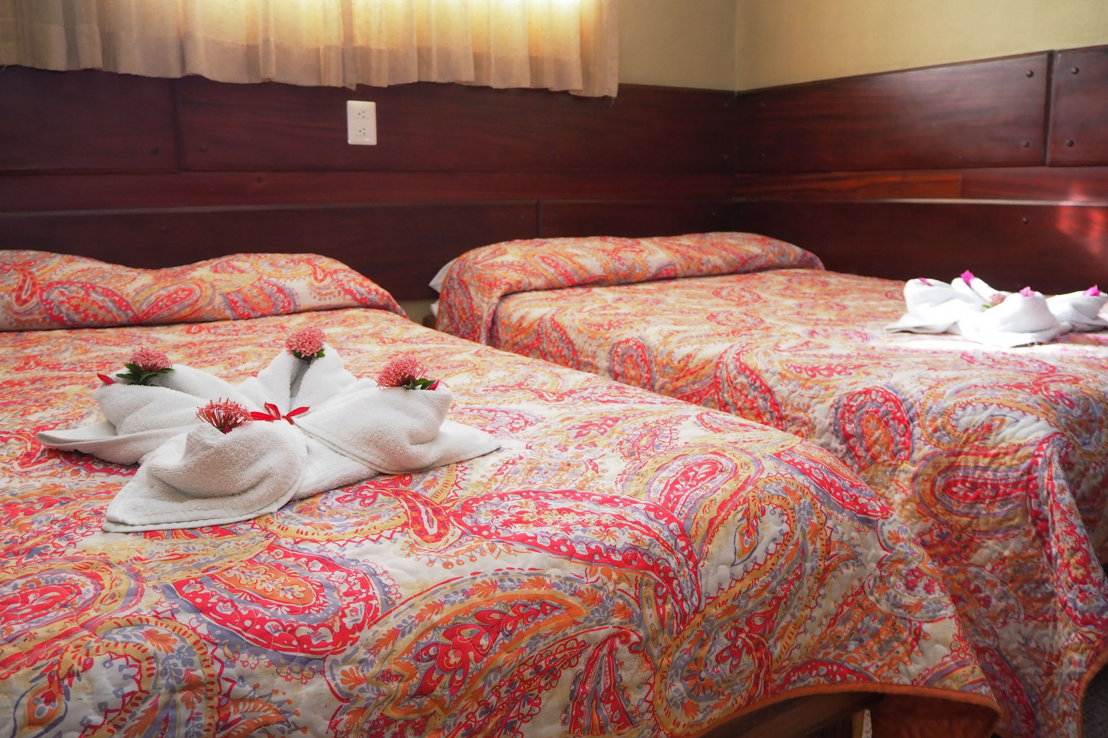A hotel room with two beds, each with a patterned bedspread and towels with flowers.
