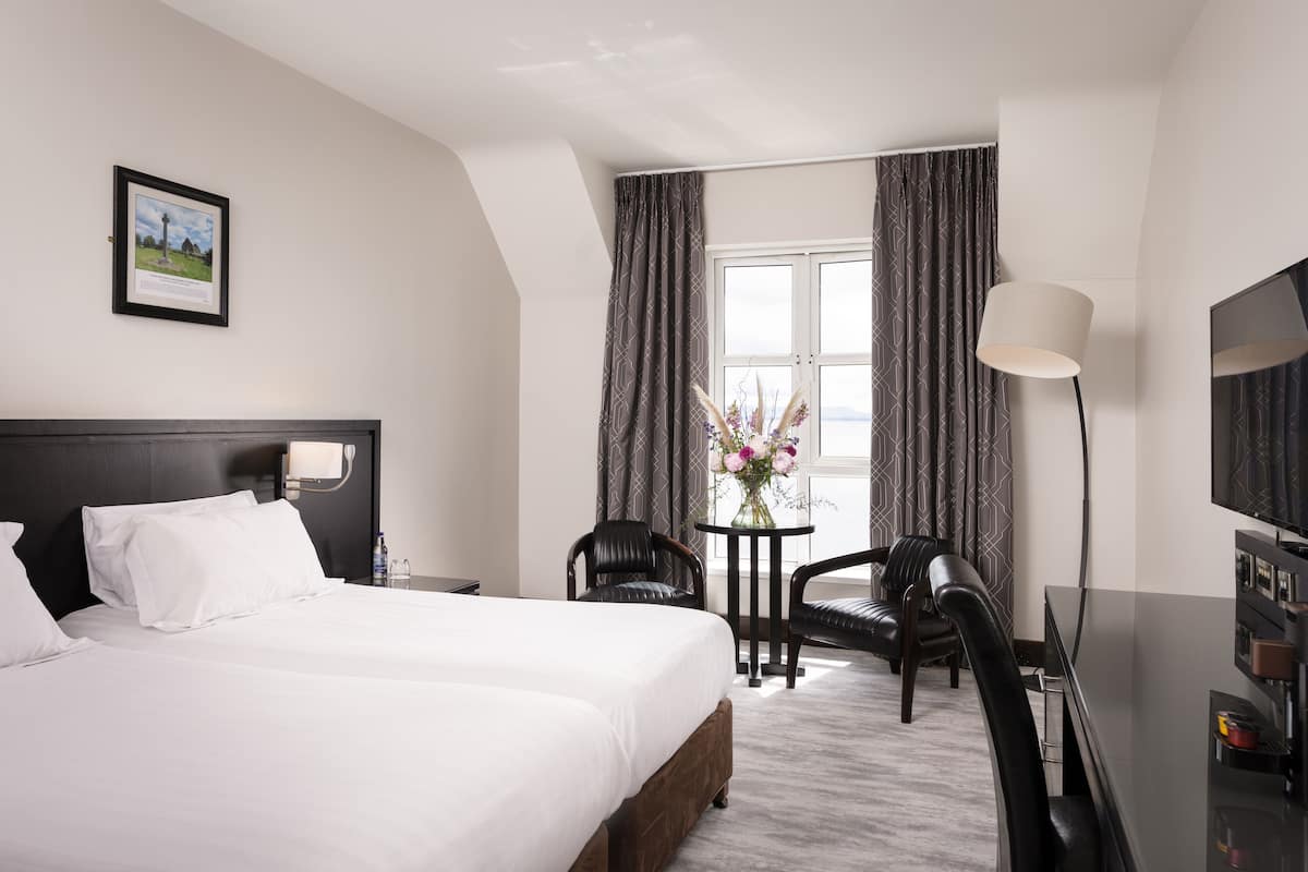 A hotel room with a large bed, a desk with a chair, a TV, and a window with curtains.