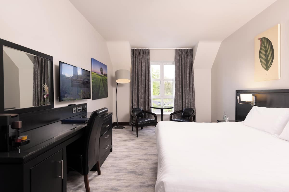 A hotel room with a bed, desk, chairs, and a large window with curtains.