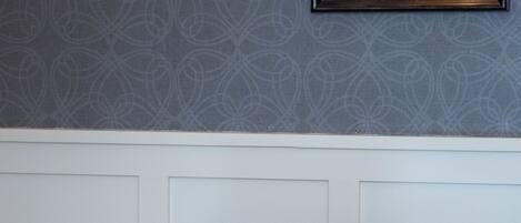 A room with a patterned wallpaper, a framed picture on the wall, and two brown leather chairs.