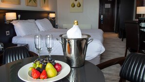 Habitación de hotel con una cama, una mesa de comedor con fruta y champán, y vista al resto de la habitación.