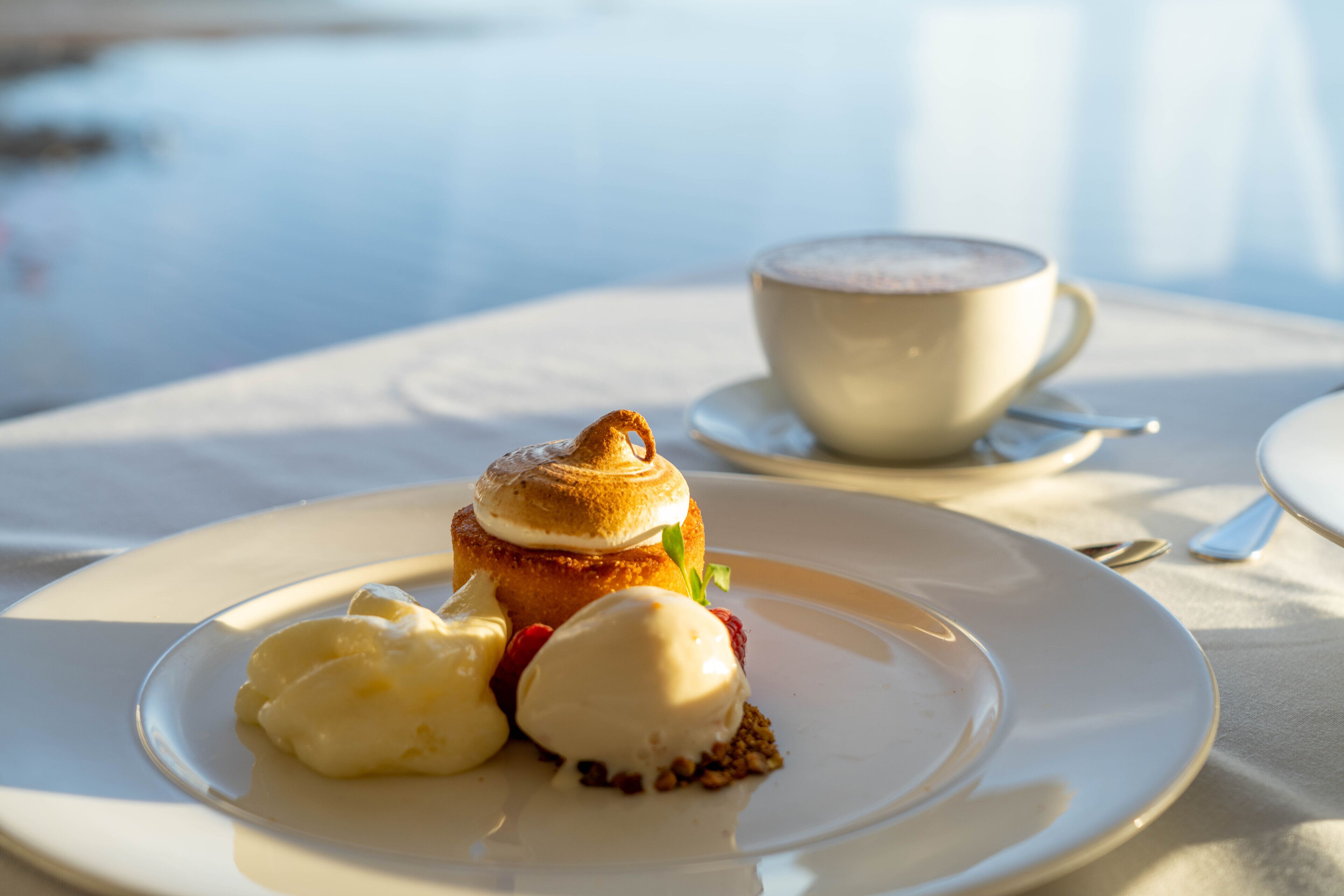 Un plato de postre con un pastel, helado y bayas sobre un mantel blanco.