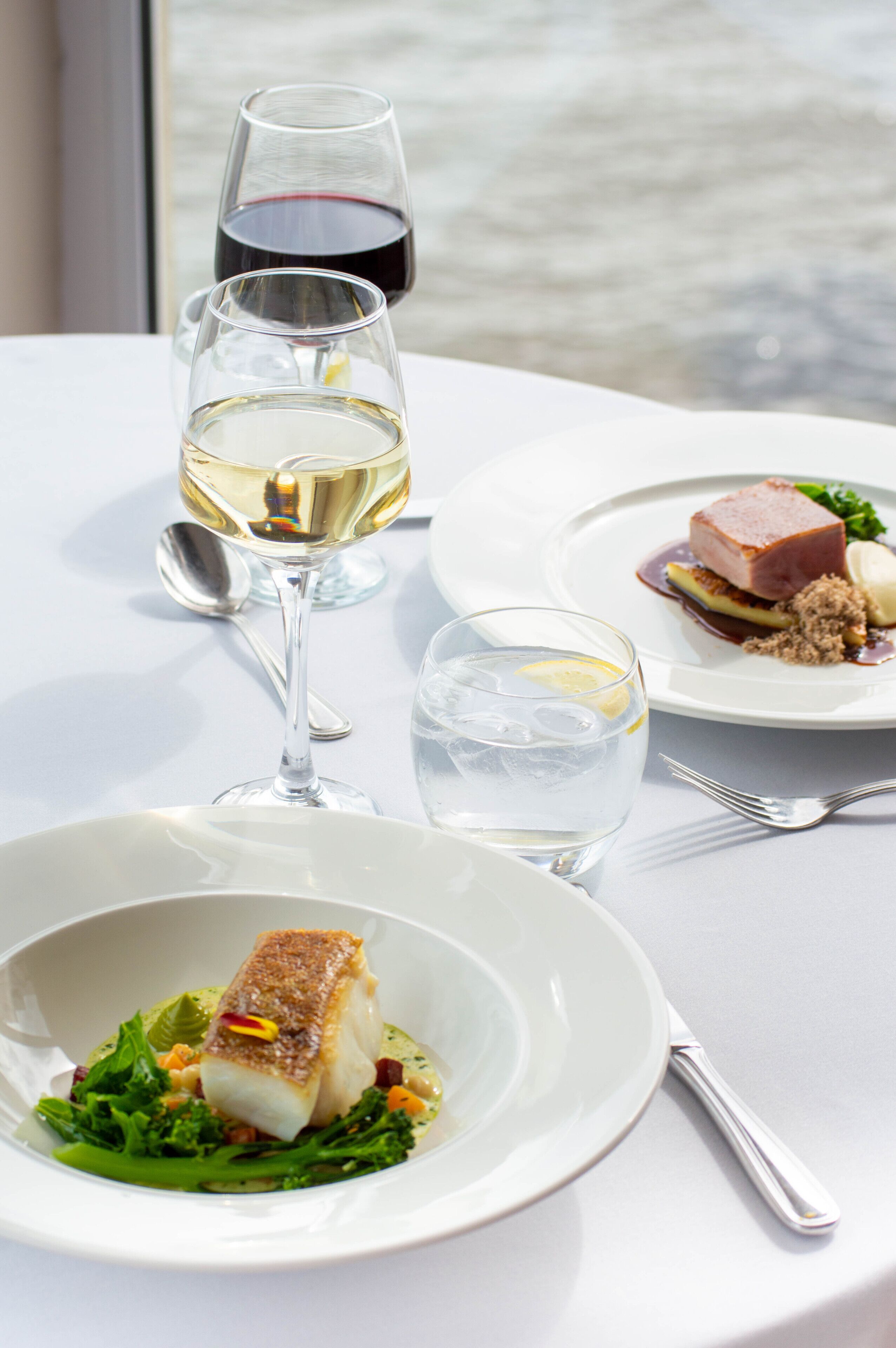 A dining table with plates of food, glasses of water and wine, and cutlery.