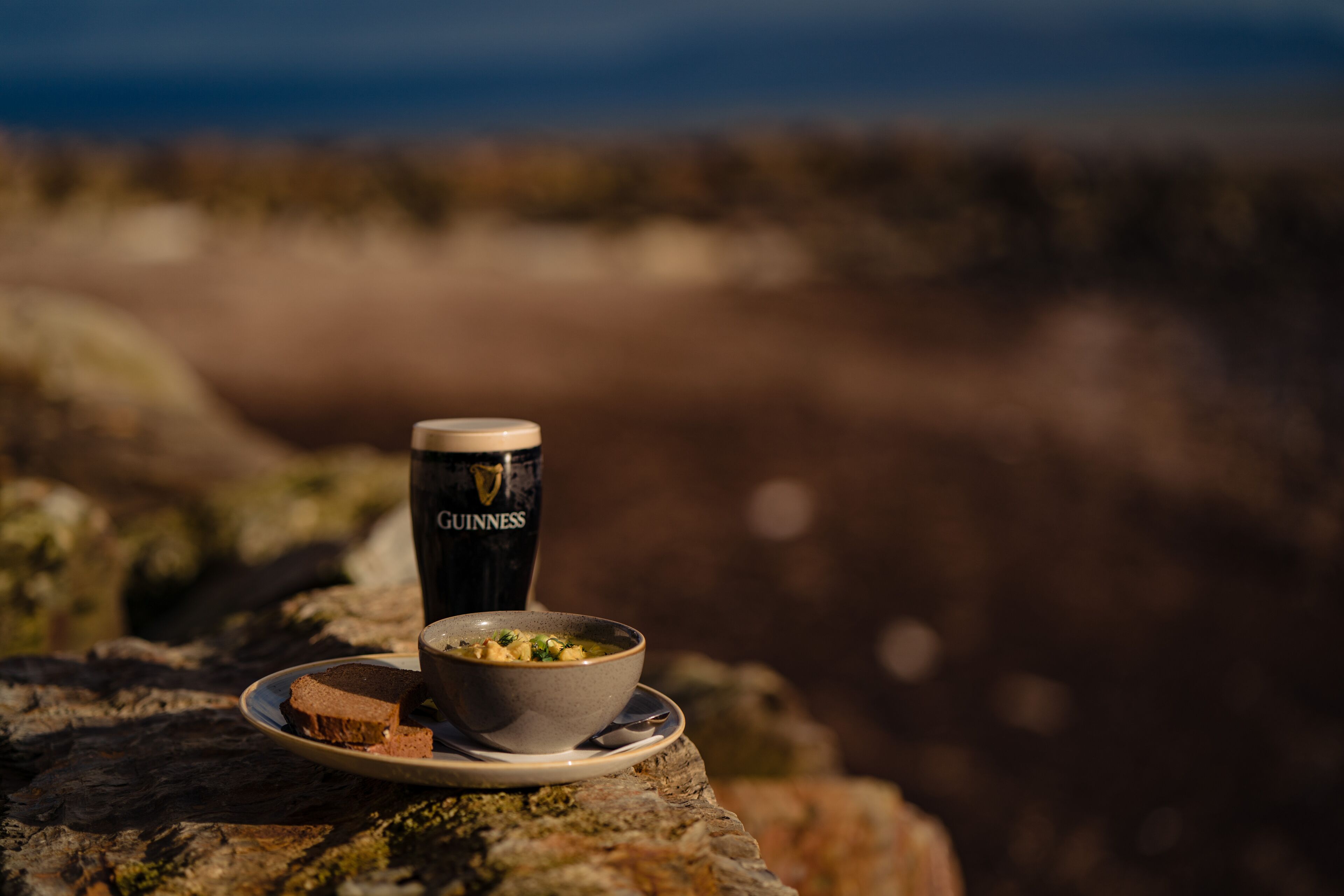 A meal of soup and bread on a rock with a Guinness beer can beside it.