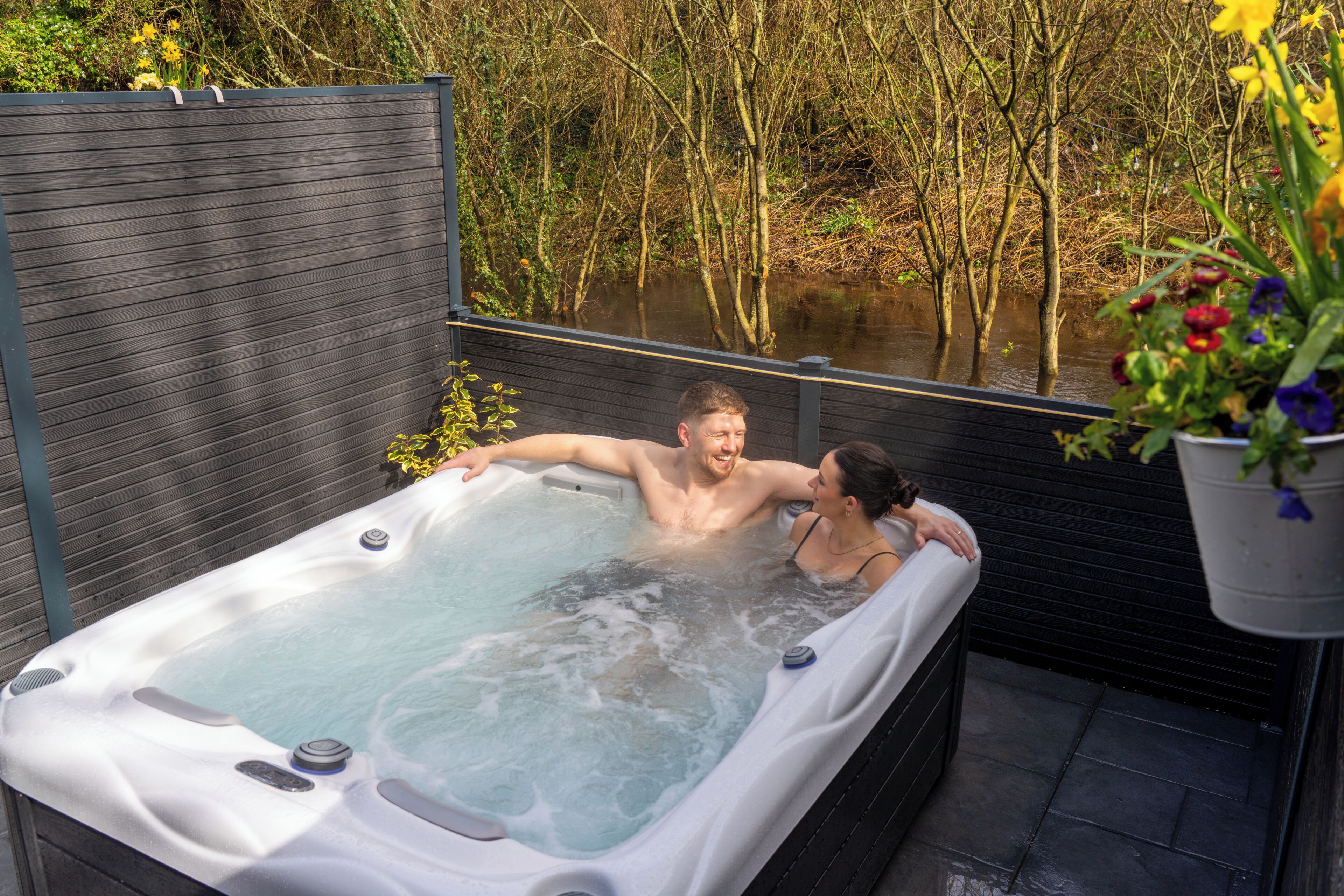 A hot tub with a wooden deck and a view of a water body.