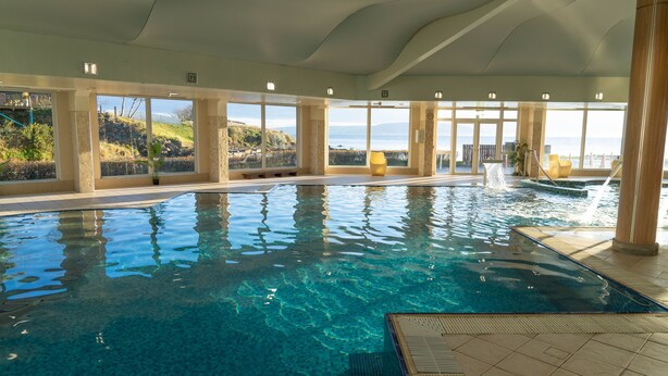 Una piscina interior con agua cristalina, grandes ventanales y vistas al exterior.