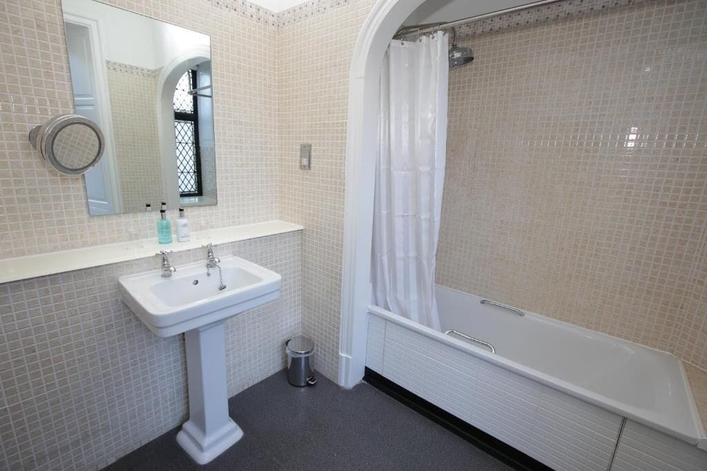 A bathroom with a pedestal sink, a mirror, a shower with a curtain, and a bathtub.