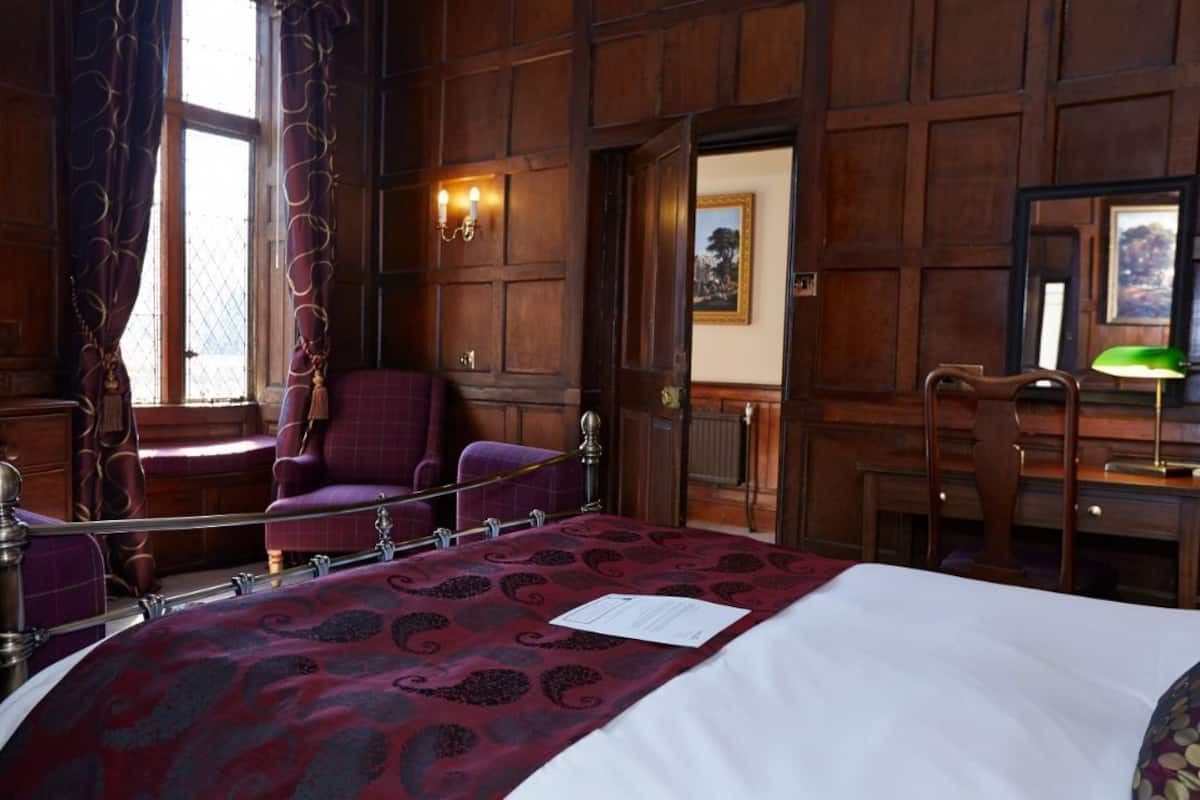 A hotel room with a large bed, a chair, a desk, and a window with curtains.