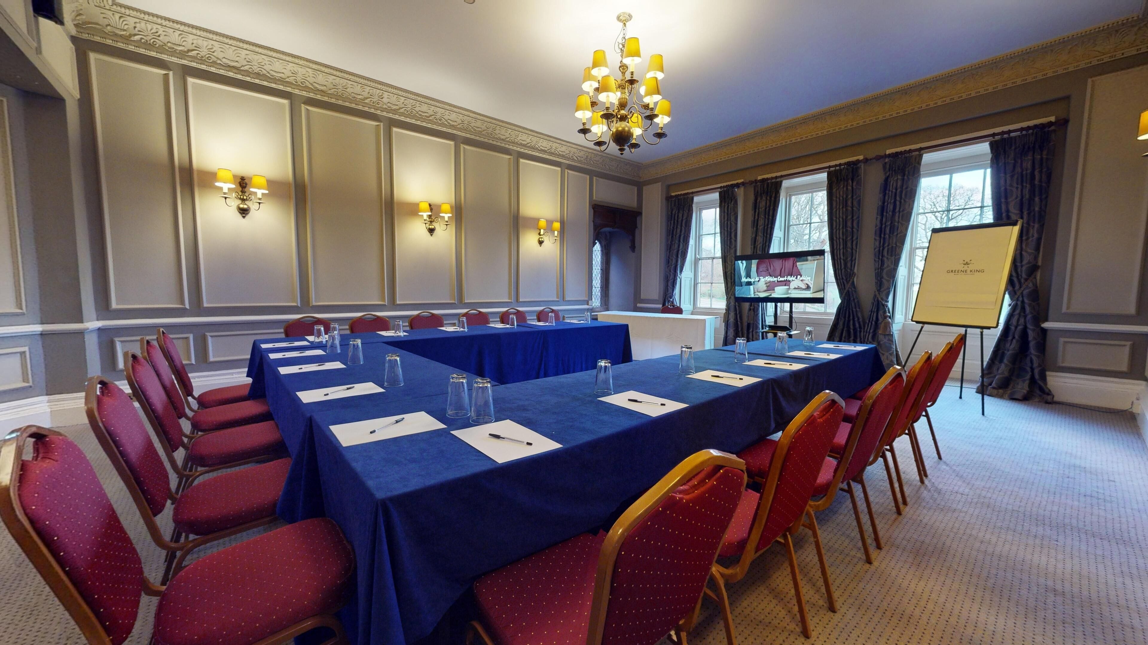 A conference room with a long table, red chairs, and a projector screen.