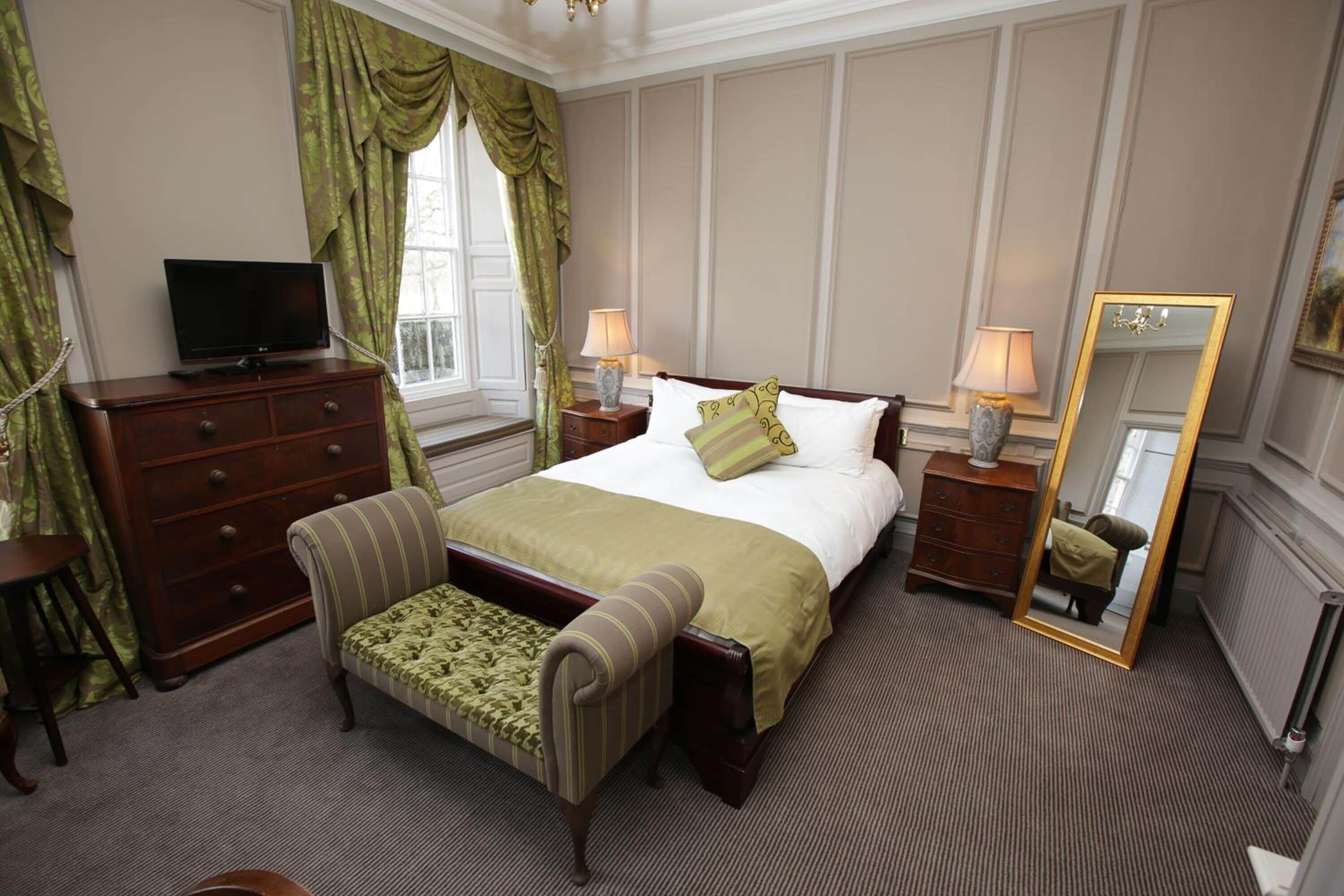 A hotel room with a bed, a television, a dresser, a chair, a mirror, and a window with curtains.