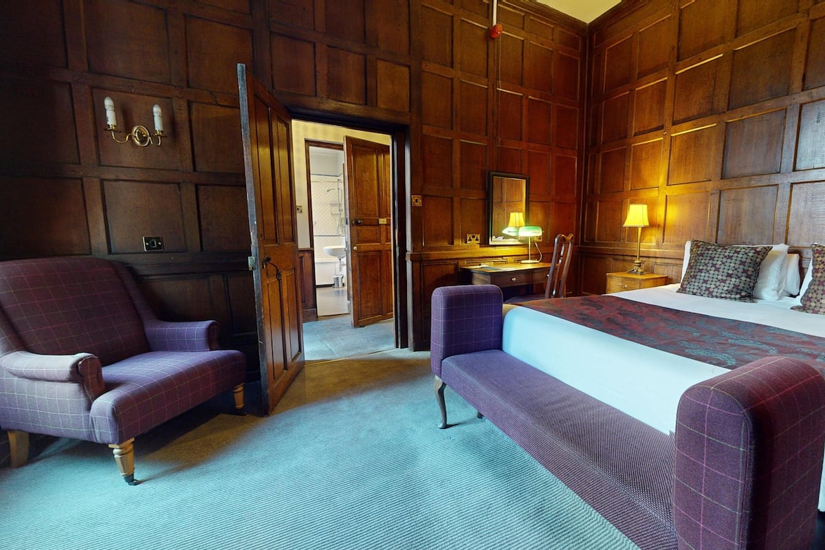 A hotel room with a large bed, two armchairs, a desk, and a mirror.