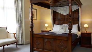 A four-poster bed with a wooden frame and a canopy, two bedside tables with lamps, a chair, and a framed picture on the wall.