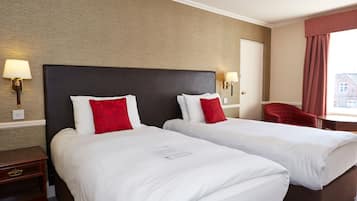 Habitación de hotel con dos camas, cada una con ropa de cama blanca y almohadas rojas, cabecero oscuro y una silla roja.