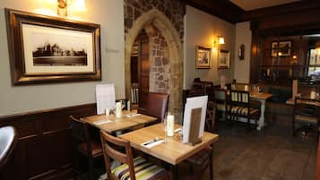 A restaurant with wooden tables and chairs, stone archway, framed picture, and a sign indicating the restroom.