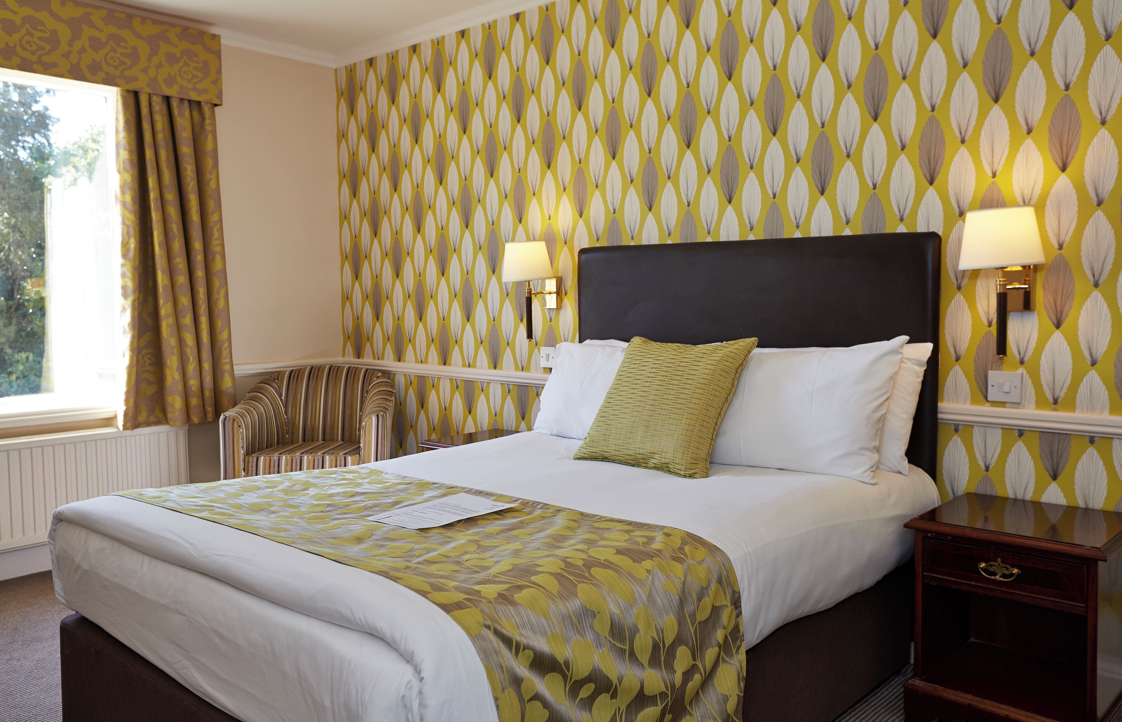 A hotel room with a large bed, two bedside lamps, a nightstand, and a window with curtains.