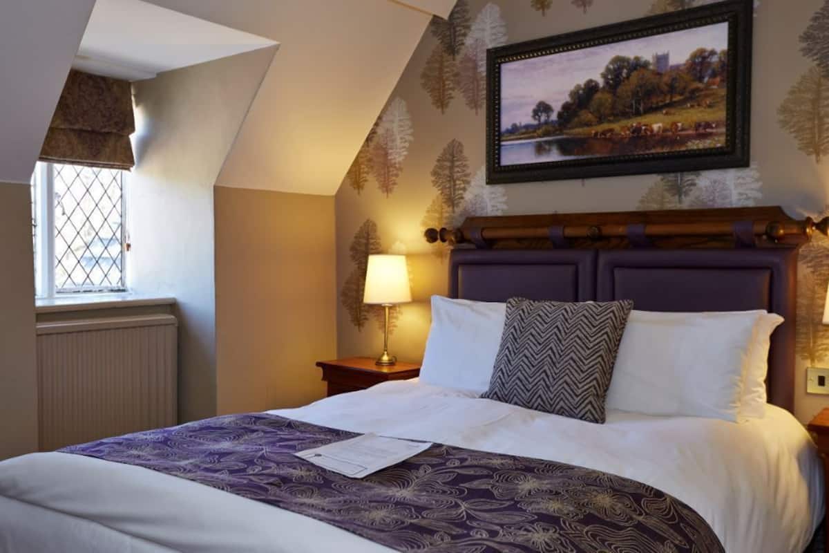 A bedroom with a large bed, a window with a view of the countryside, and a framed picture on the wall.
