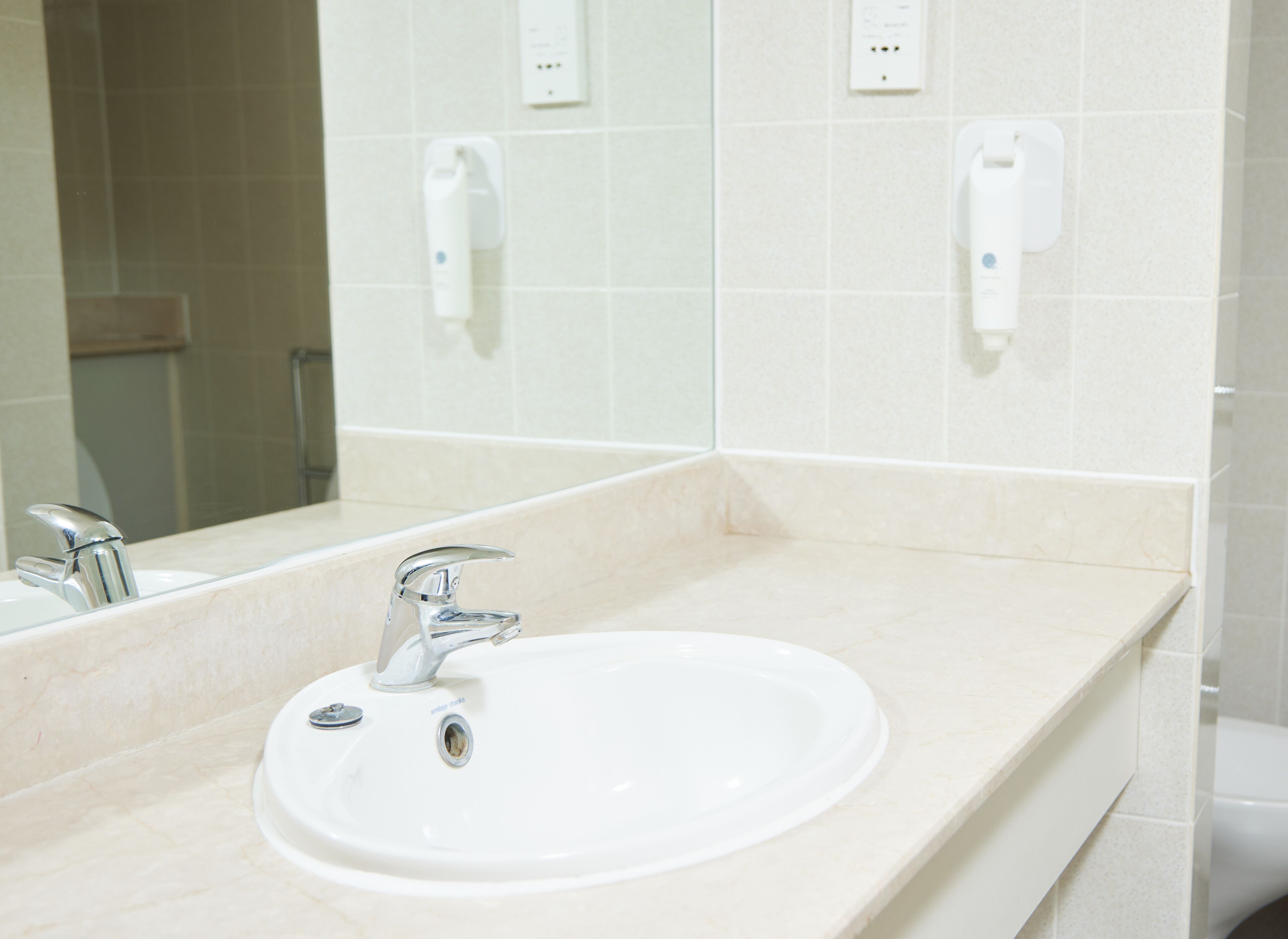 Un baño con lavamanos, espejo y dos secamanos en la pared.