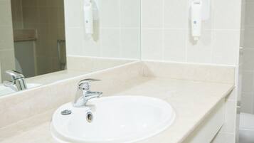 Un baño con lavamanos, espejo y dos secamanos en la pared.