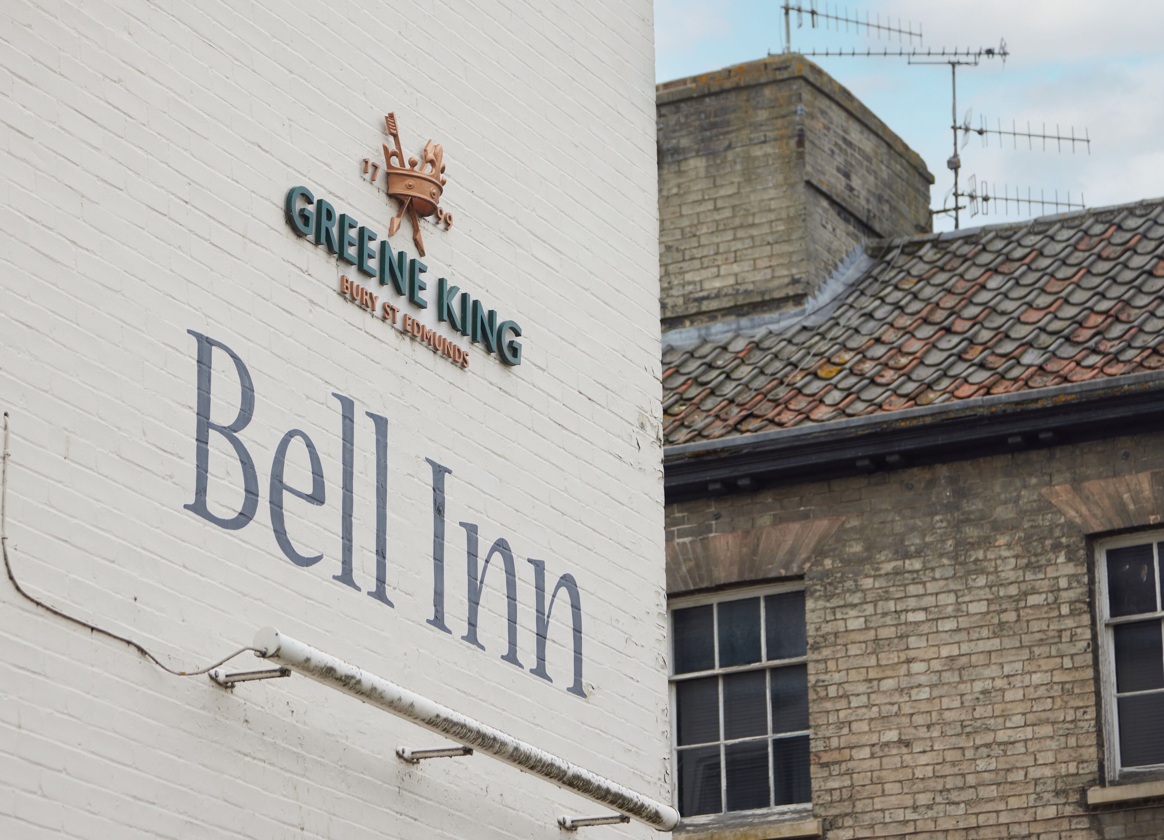 Ein Gebäude mit einem Schild für das 'Green King Bell Inn' und einem Kronen-Emblem.