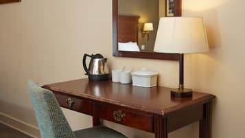 A wooden desk with a lamp, a kettle, and a chair in a hotel room.