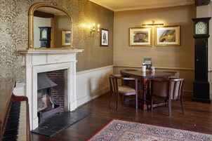 Una habitación con chimenea, una mesa de comedor con sillas, un reloj y cuadros en la pared.