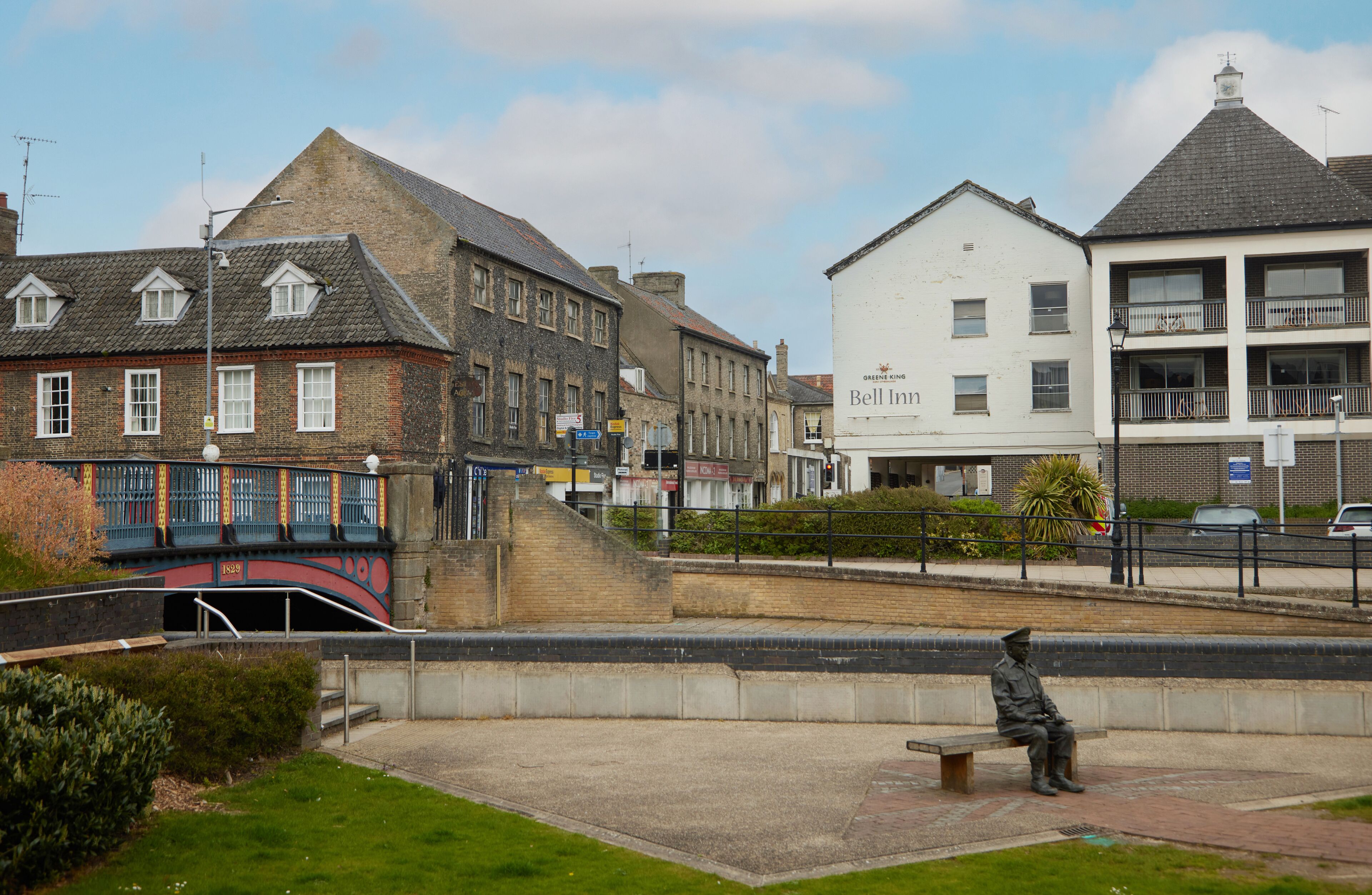 A historic building with a traditional brick facade, a small bridge, and a statue of a soldier on a bench.