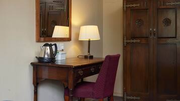 A wooden desk with a lamp, a chair, and a mirror reflecting a cabinet.