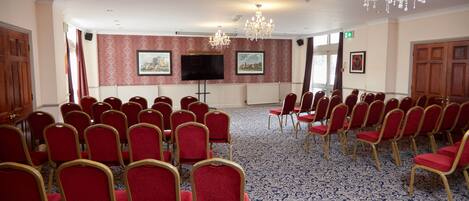 A conference room with rows of red chairs, a large screen, and a chandelier.