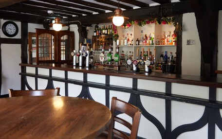 A bar area with wooden furniture, a clock, and shelves with bottles and glasses.