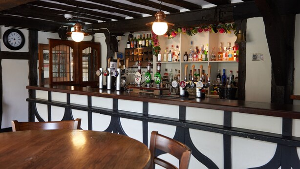 A bar area with wooden furniture, a clock, and shelves with bottles and glasses.