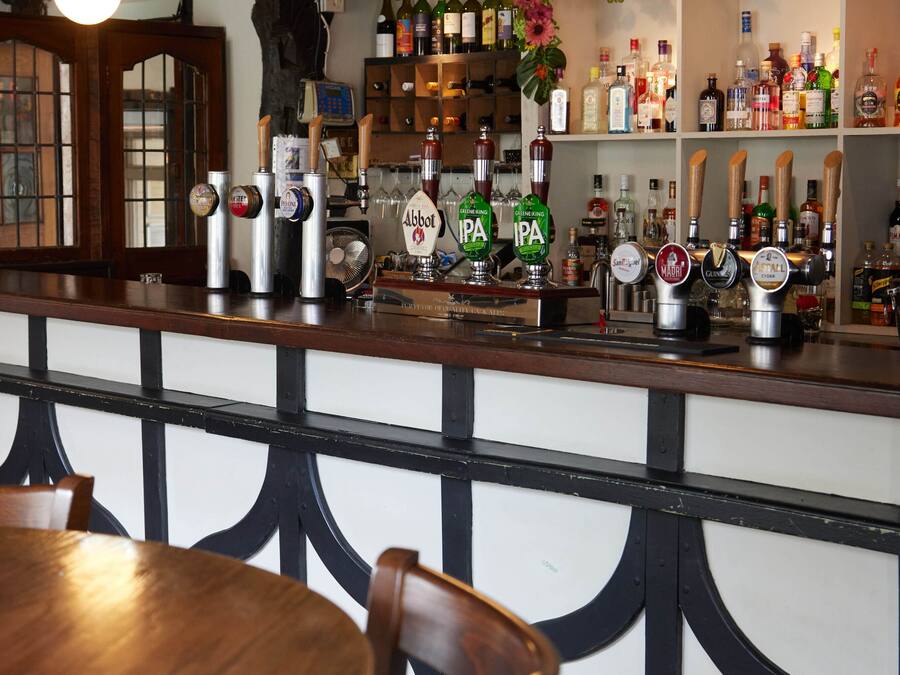 Zona de bar con muebles de madera, una barra con grifos y estantes llenos de botellas.