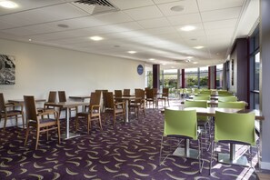 A dining area with tables and chairs, a patterned carpet, and large windows. - Holiday Inn Express Dunstable by IHG (Dunstable)