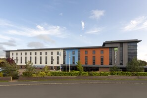Un bâtiment moderne aux façades aux couleurs variées, allant du blanc au bleu en passant par l’orange, sur lequel on peut voir une enseigne Holiday Inn Express.