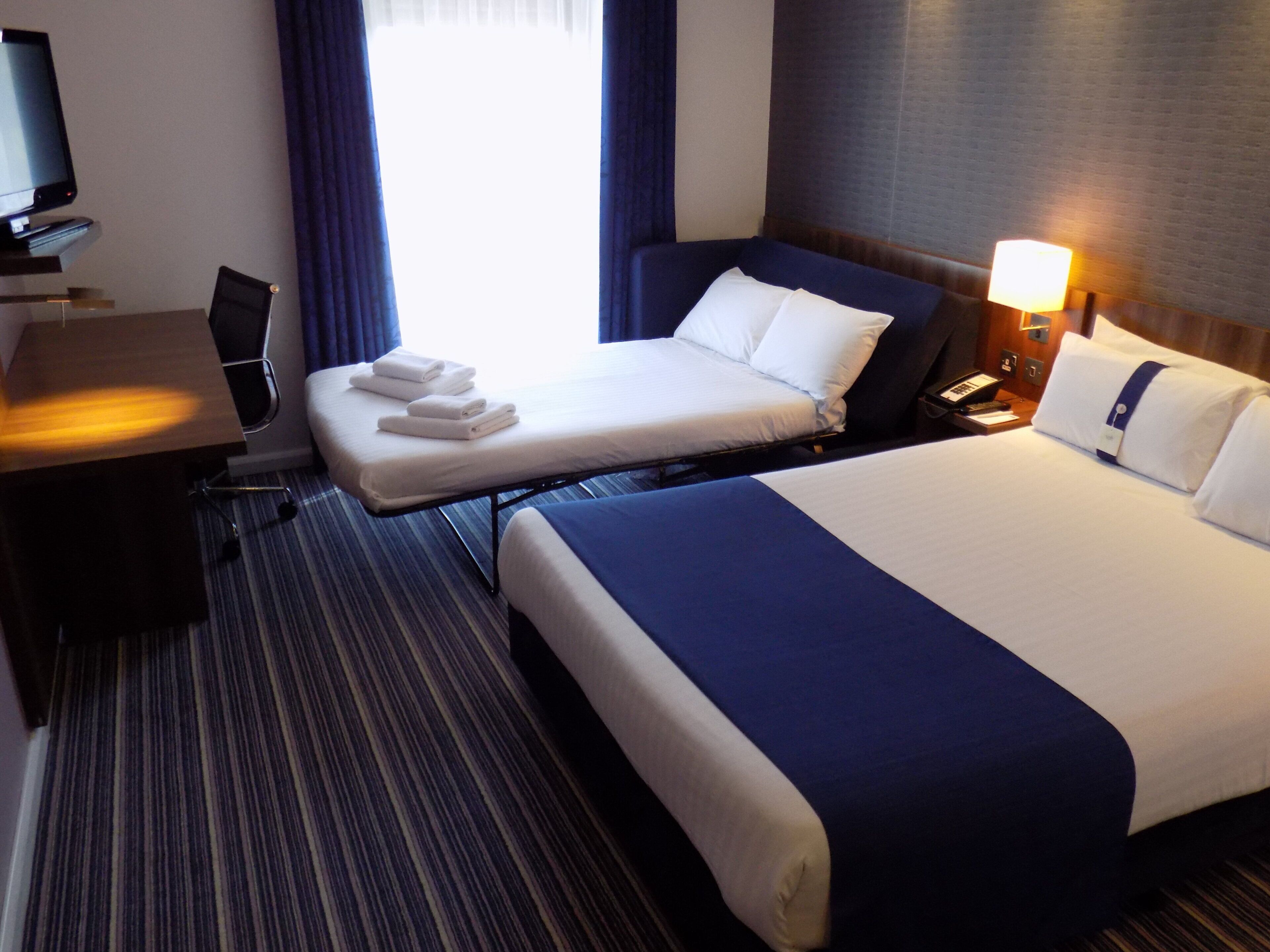 Una habitación de hotel con cama, escritorio, silla y televisión.