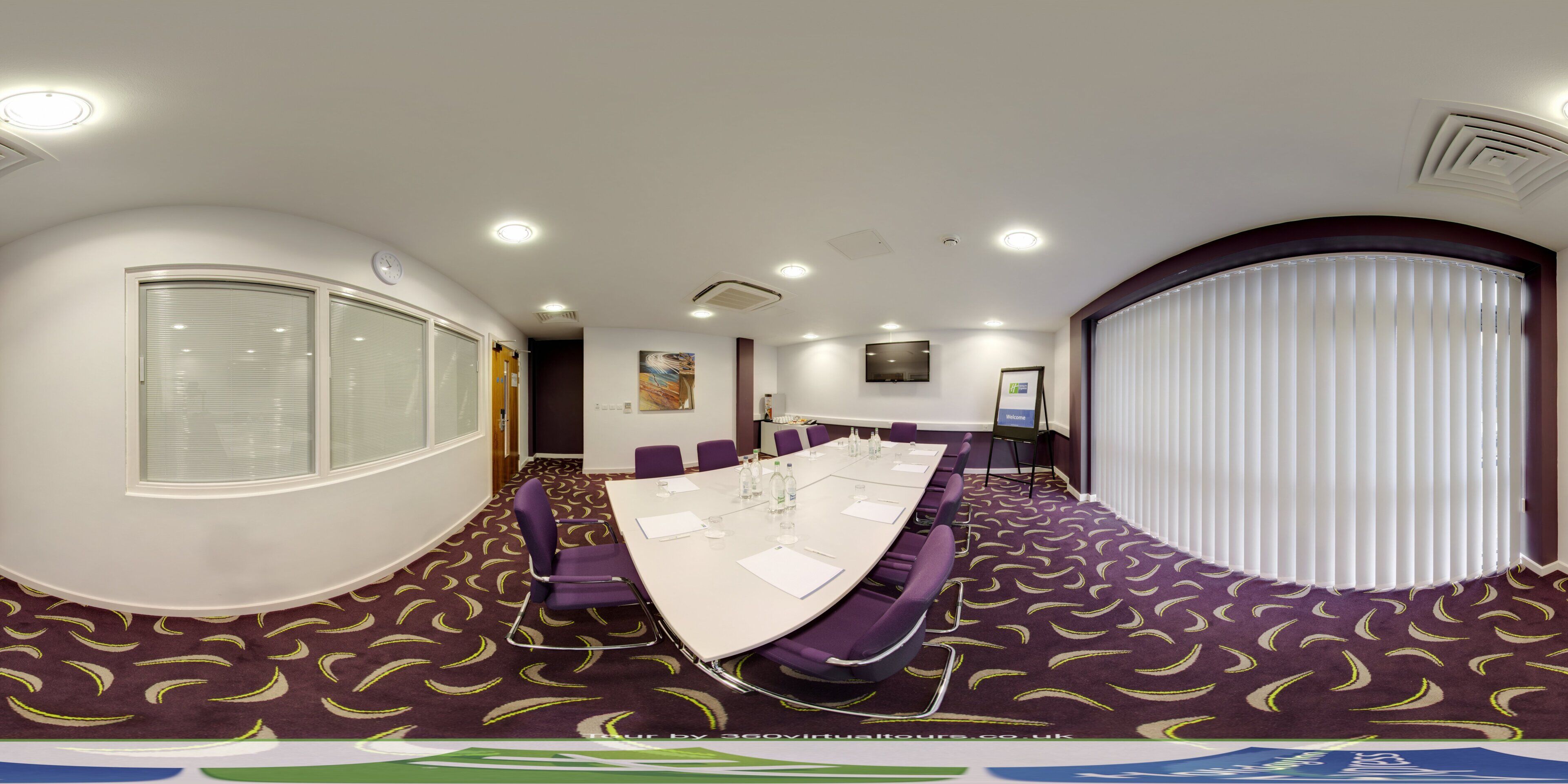 A conference room with a long table, purple chairs, and a large window with blinds.