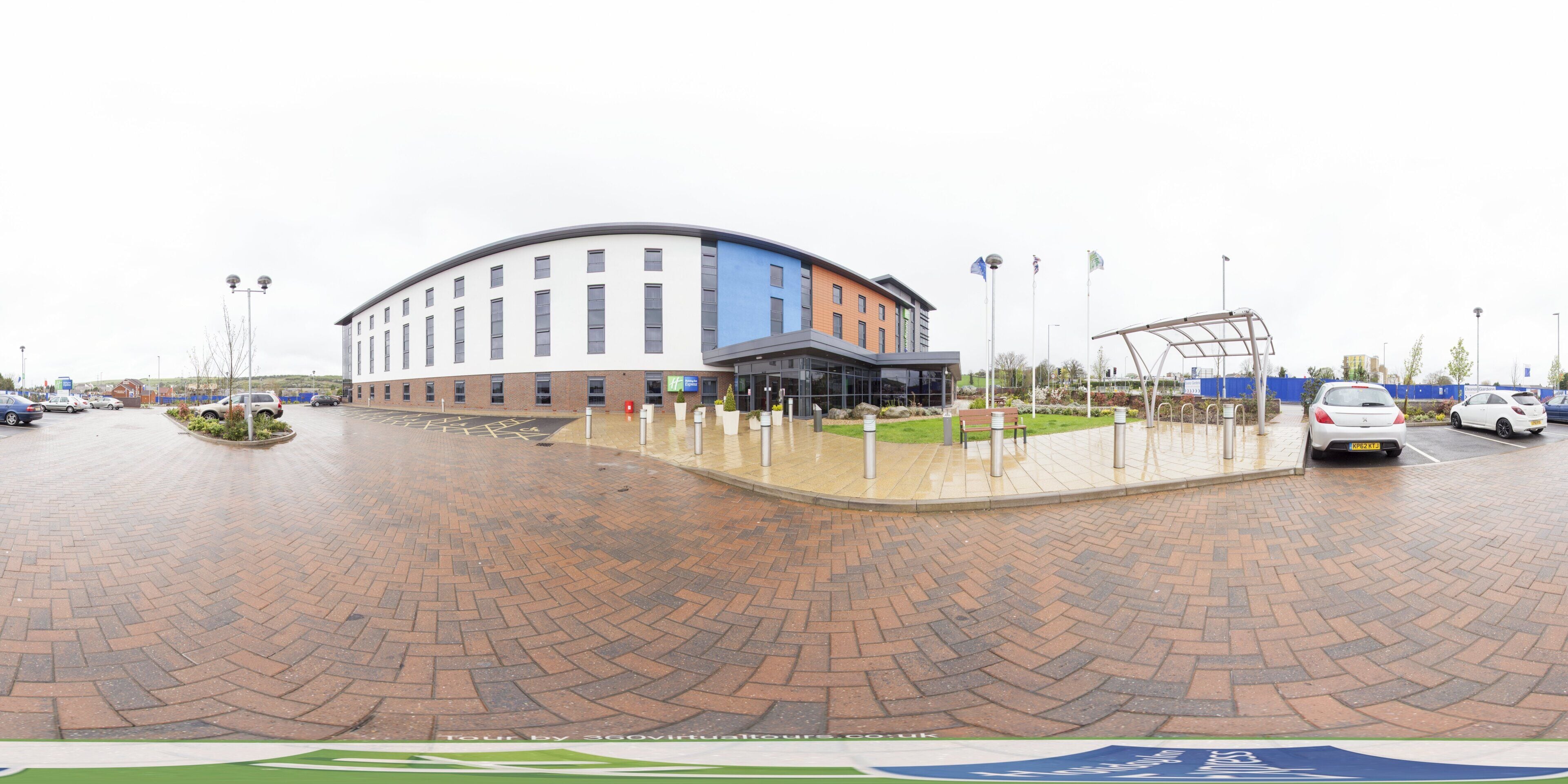 A modern building with a curved facade, a parking area with cars, and a landscaped garden.
