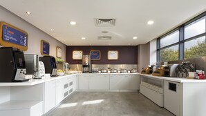 A modern kitchen with a coffee station, breakfast sign, and a view of the outdoors through large windows.
