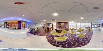 Un moderno vestíbulo de hotel con una recepción, zona de estar y vistas de la ciudad a través de amplios ventanales.