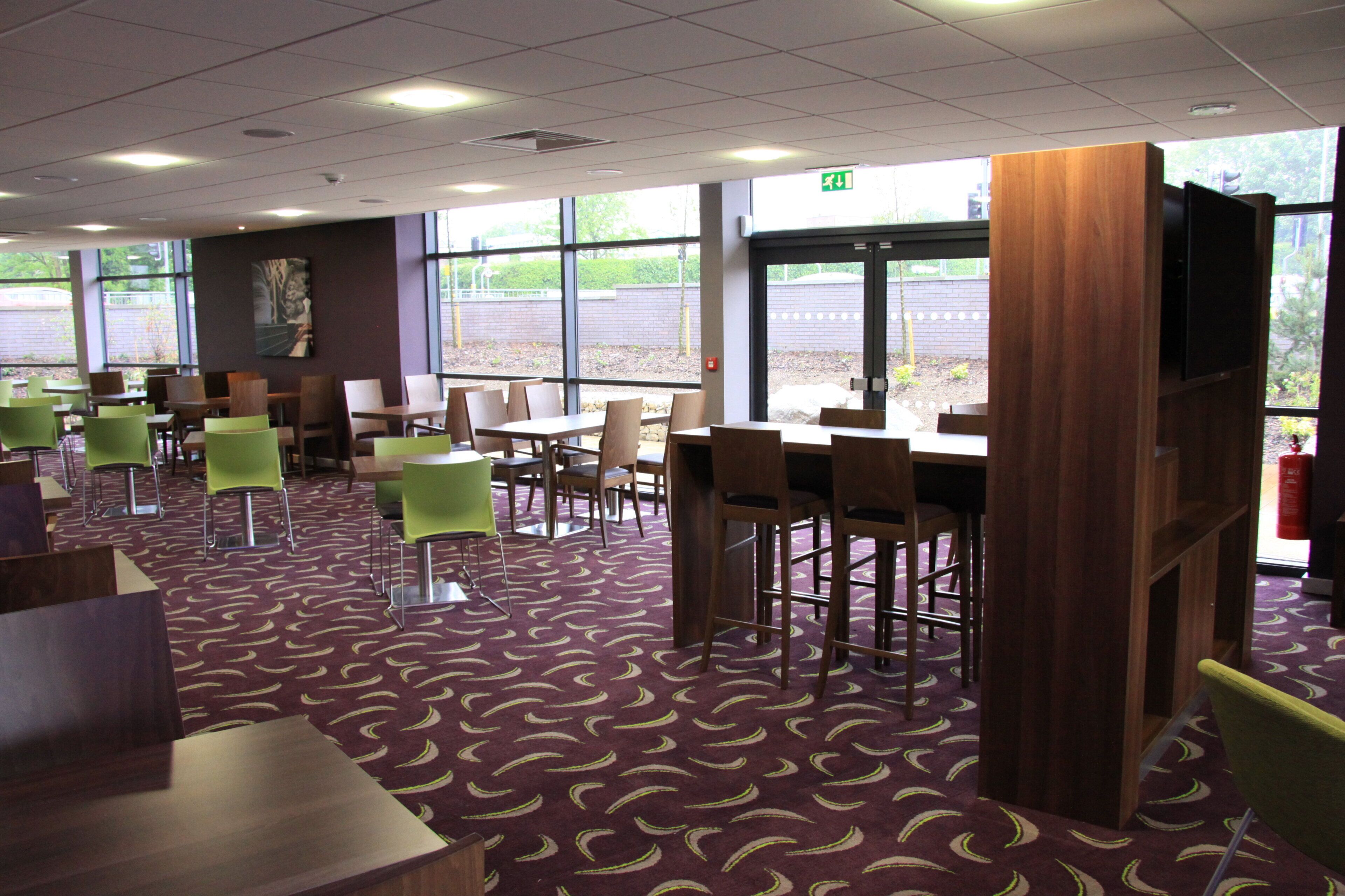 A restaurant with high tables and chairs, a patterned carpet, and large windows.