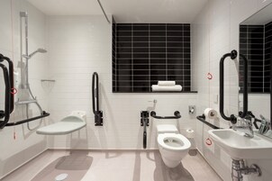 Un baño moderno con ducha, inodoro y lavamanos, equipado con barras de apoyo y pasamanos.