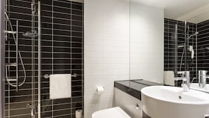 Et moderne badeværelse med en glasbrusekabine, et hvidt toilet, en stor vask og et spejl.