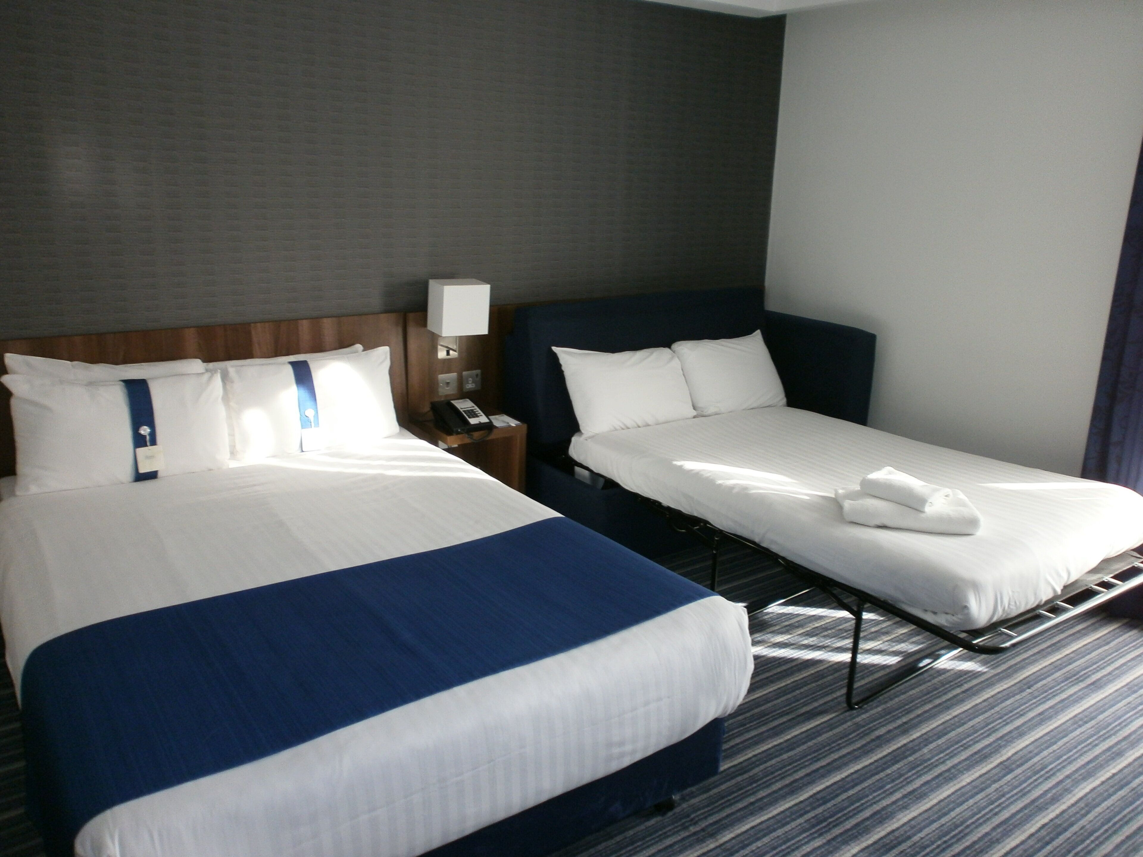 A hotel room with two beds, a nightstand, a lamp, and a telephone.