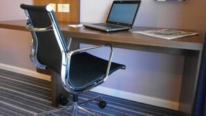 Et hotelværelse med et skrivebord, en bærbar computer, en stol og et lille bord.