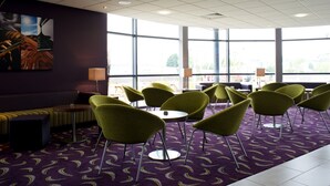 A hotel lobby with a purple carpet, green chairs, a sofa, and large windows.